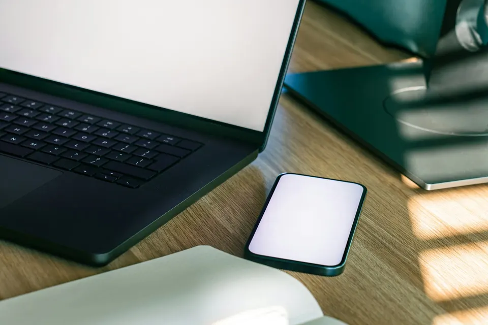 A smartphone with a blank screen beside a laptop on a desk