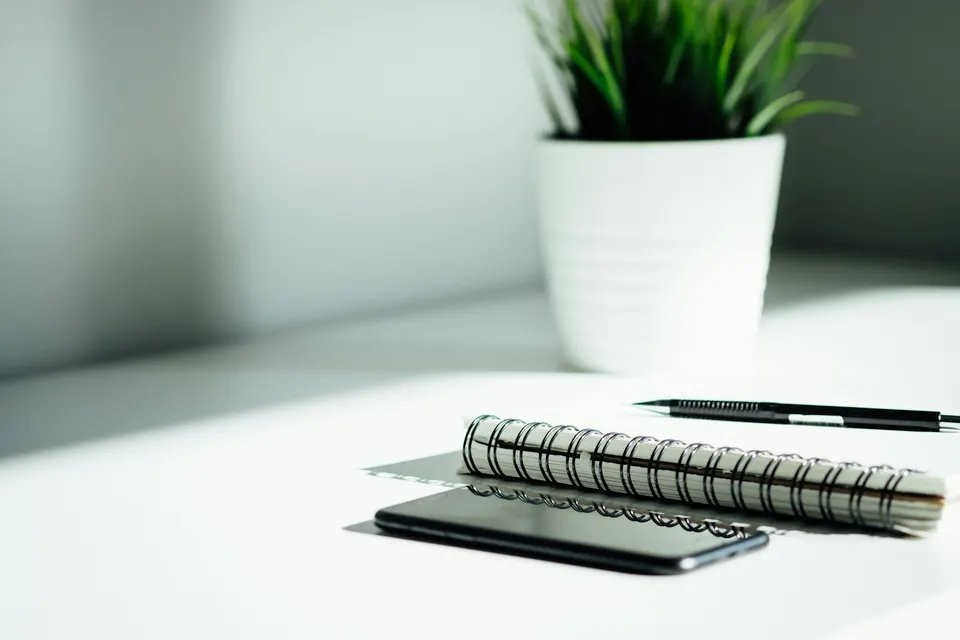 A notebook, phone and pen on a light desk